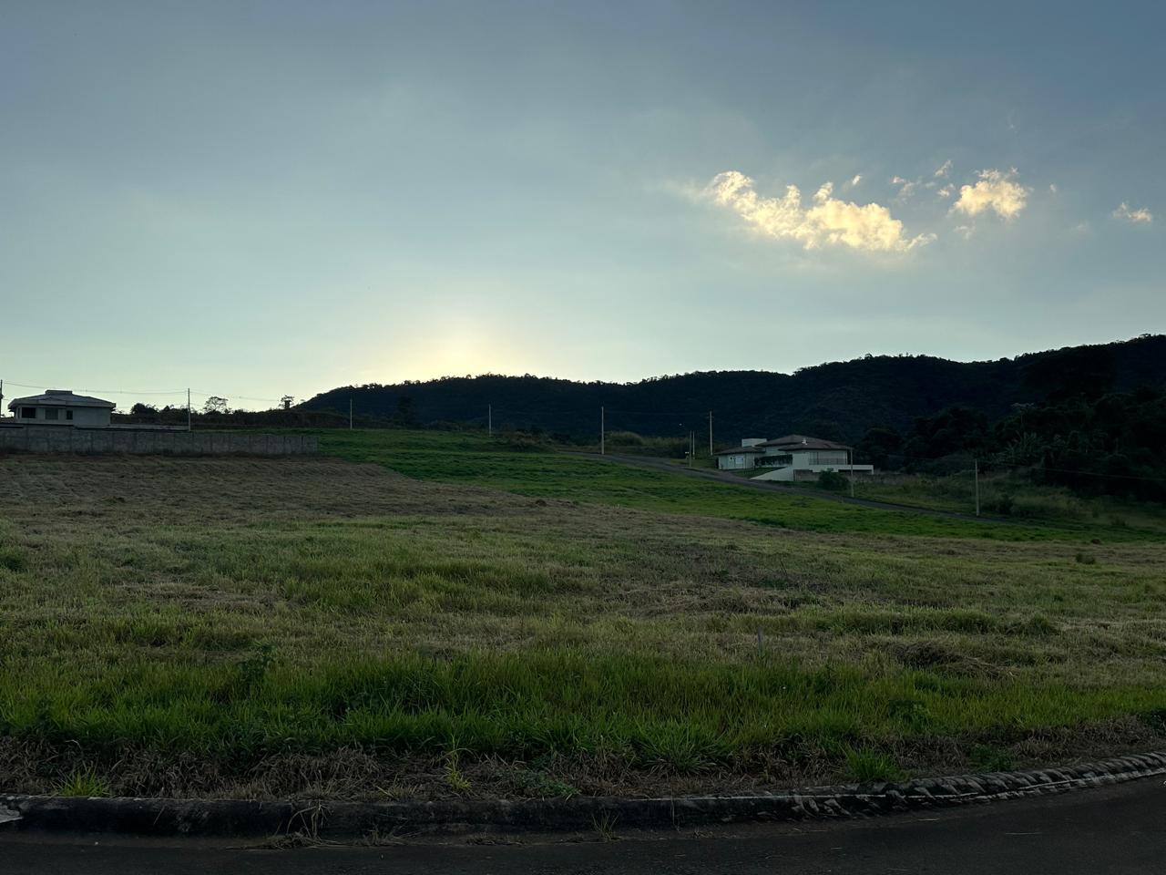 Vista ampla dos lotes limpos do condomínio com o sol se pondo atrás dos morros